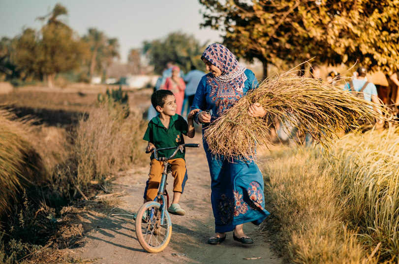 Female farmer waling with her son while carrying crops