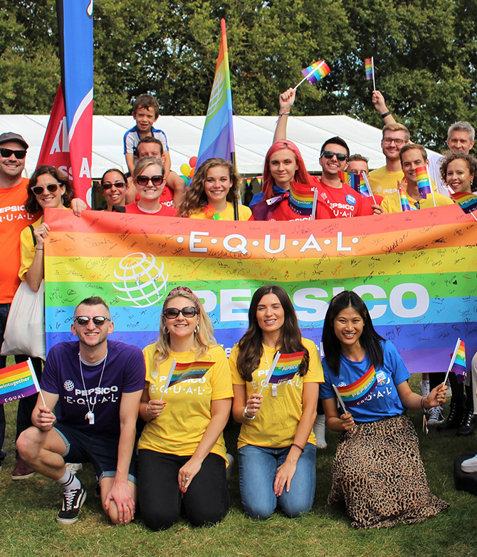 Lively group of 25 men, women, and children outdoors and in rainbow attire celebrating Pride at Pepsi with banners and flags. | LGBTQ