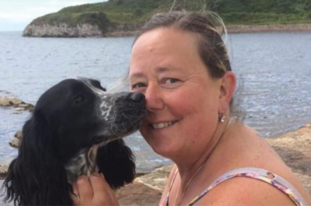 Amanda smiles as she sits at the lake with her dog, who is nuzzling her face with his nose. | Mental Health