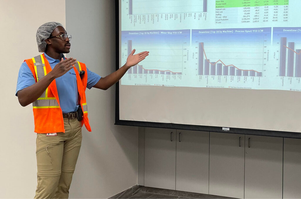 STEM Leader Demi Oyeniyi wears an orange reflective vest as he goes over a presentation in the workplace